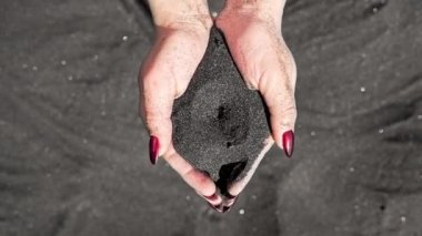 Kadın eli volkanik siyah kumu yavaşça parmaklarından akan tropik ada sahilinde. Gün batımında kırmızı tırnaklı genç bir kadının kumla oynadığı güzel bir sahne..