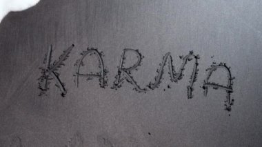 Karma kelimesi siyah kumsalda yazılmış, deniz veya okyanus dalgalarıyla sürüklenmiş. Sebep ve sonuç. Din kavramı, ezoterizm, Budizm, dünya uyumu ve evren dengesi.