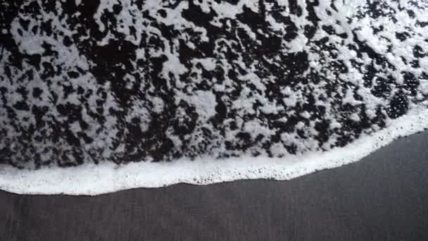 Svart kanariefågel sand strand bakgrund. Vulkanisk grus sköljs av vågor av hav. Fantastisk natur scen Bali ö plage med vulkan. — Stockvideo