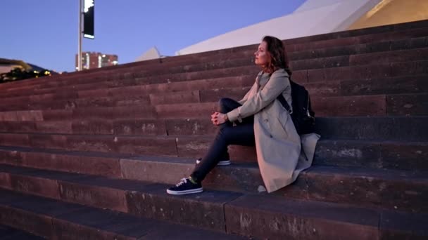 Mulher muito viajante com mochila sentada nas escadas do Auditório em Santa Cruz de Tenerife. Bela arquitetura moderna. Retrato de menina relaxante ao ar livre na cidade. — Vídeo de Stock