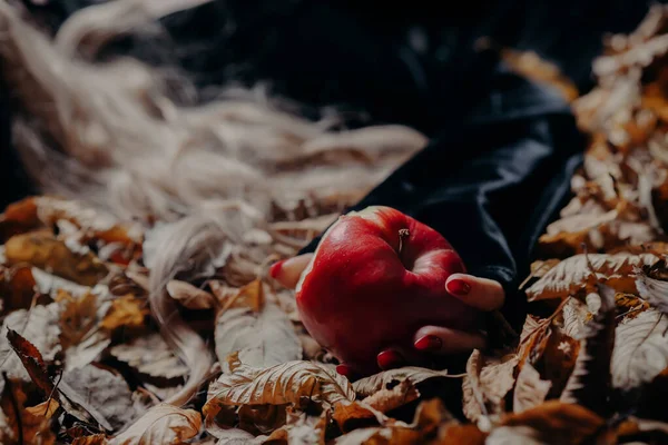 Woman snow white poisoned by apple lies on ground in forest. Symbol of temptation, poison. Fairy tale, wizard, toxic concept. Spooky halloween, cosplay.