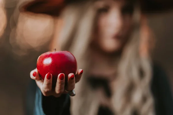 Witch woman in black offers red apple as symbol of temptation, poison. Fairy tale, white snow wizard concept. Spooky halloween, cosplay. — Foto Stock