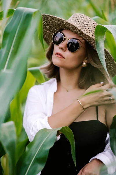 Portrait of young stylish woman in green jungle. Girl in straw hat and sunglasses, linen clothes. Lady looks happy and healthy, she smiles. — Foto Stock