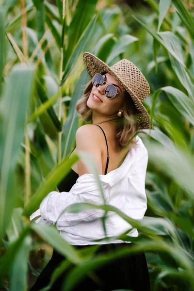 Portrait of young stylish woman in green jungle. Girl in straw hat and sunglasses, linen clothes. Lady looks happy and healthy, she smiles. — Foto Stock