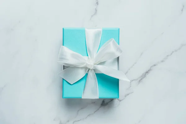 Elegante caja azul regalo de lujo atada con cinta de seda sobre fondo de mármol blanco. Regalo de cumpleaños, aniversario, tarjetas, postales, concepto de papel pintado. — Foto de Stock