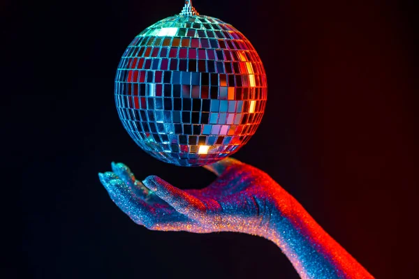 Glitter vrouwelijke hand houden spinnen disco spiegel bal onder neon. Glanzende zilveren bol reflecteert licht. Retro avond feest, muziek en entertainment concept achtergrond — Stockfoto
