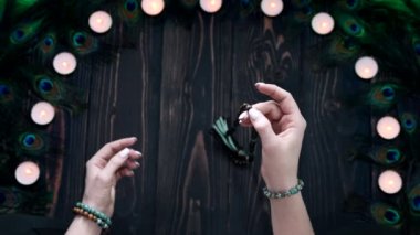 Mantraları ya da duaları okuyan kadın meditasyonlar sırasında kullanılan tahta boncukları sayıyor. Bayan mumların ve tavus kuşu tüylerinin arasında oturuyor. Maneviyat, din, Tanrı kavramı..