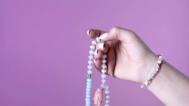 女性ライトハンドは、マントラ瞑想中にカウントを維持するために使用される宝石のマラビーズのストランドをカウントします。ピンクの背景。精神性、宗教、仏教の概念. — ストック動画