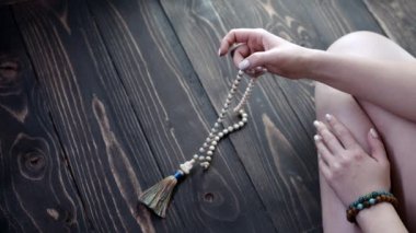 Kadın el feneri, mantra meditasyonlar sırasında saymak için kullanılan değerli taşların kollarını sayıyor. Bayan ahşap zeminde oturuyor. Ruhanilik, din, Tanrı kavramı. Boşluğu kopyala