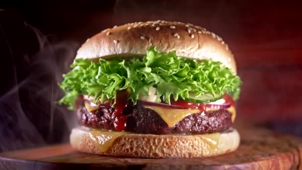 Hamburger gustoso con fumo, concetto di fast food. Hamburger fresco fatto in casa alla griglia con polpettine di carne, pomodori, cetrioli, lattuga, cipolla e semi di sesamo. Stile di vita malsano. Contesto alimentare. — Video Stock
