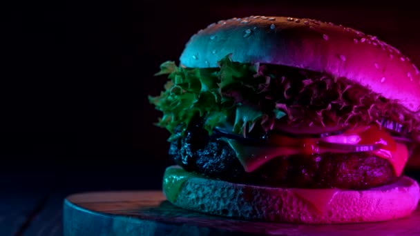 Смачний бургер під яскравим неоновим світлом, швидка їжа концепції. Свіжі саморобні гримучі гамбургери з м'ясом, помідорами, насінням кунжуту. Нездоровий спосіб життя. Нічна їжа. Постріл Доллі. — стокове відео