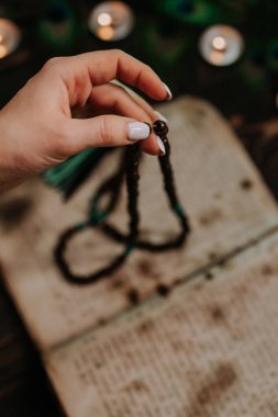 Mantralar ya da antik kutsal kitaptan dualar okuyan kadın, meditasyonlar sırasında kullanılan tahta boncuk ipliklerini sayıyor. Bayan mum ve tavus kuşu tüylerinin arasında oturuyor. Maneviyat, din, Tanrı kavramı..
