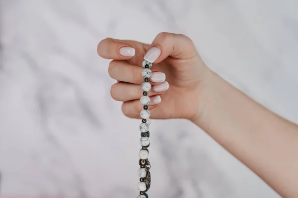 La main éclairée de la femme compte les brins de perles de mala de pierres précieuses utilisées pour compter pendant les méditations du mantra. Fond de lumière en marbre. Spiritualité, religion, concept de Dieu. — Photo