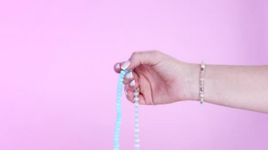 Kadın eli, mantra meditasyonlar sırasında saymak için kullanılan değerli taşların kollarını sayıyor. Pembe arka plan. Maneviyat, din, Tanrı kavramı..