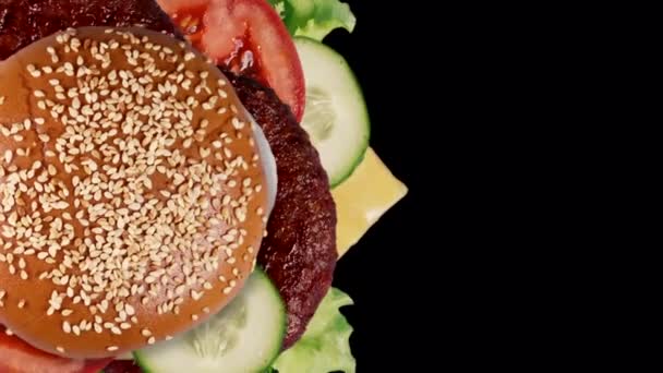Komponen burger segar Yummy berputar terisolasi pada hitam, konsep makanan cepat saji. Salin ruang. Patty daging, tomat, mentimun, selada, bawang, biji wijen. Screensaver untuk restoran. — Stok Video
