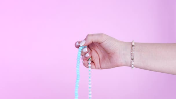 女性の手は、マントラ瞑想中にカウントを維持するために使用される宝石のマラビーズの鎖をカウントします。ピンクの背景。霊性、宗教、神の概念. — ストック動画