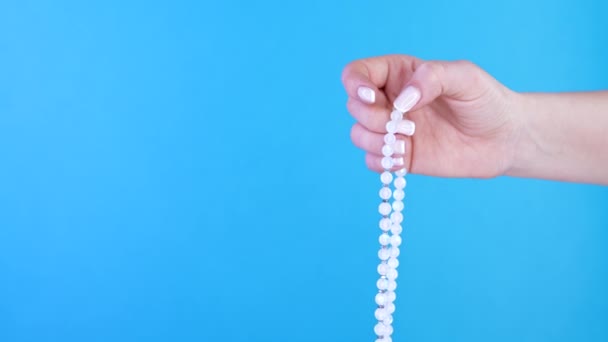 La main éclairée de la femme compte les brins de perles de mala de pierres précieuses utilisées pour compter pendant les méditations du mantra. Fond bleu. Spiritualité, religion, concept de Dieu. — Video