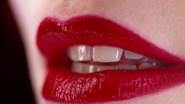 Close-up de mulher sexy morde seus lábios vermelhos com desejo. Expressão facial sensual sedutora. Flerte, sorriso, maquiagem brilhante — Vídeo de Stock
