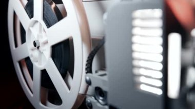 Dönüşümlü beyaz makaralar. Analog oynatıcı. Eski moda 8mm film projektörü ev sinemasında karanlıkta oynuyor. Eski nesneler, sinema, sinematograf konsepti