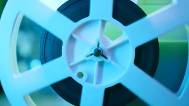 Retro eski moda 8 mm 'lik projektör kaset filmiyle makara oynuyor. Renkli ışık altında dönen bobin yakın plan. Eski nesneler, eğlence, nostalji, festival ekipmanları