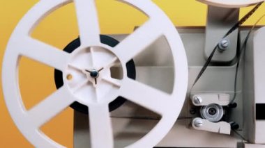 Sarı stüdyo arka planında dönen bir film makarası. Eski moda 8 mm film projektörü oynuyor. Klasik film nesneleri, nadir bulunan konsept
