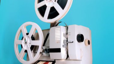 Mavi stüdyo arka planında dönen bir film makarası. Eski moda 8 mm film projektörü oynuyor. Klasik film nesneleri, nadir bulunan konsept
