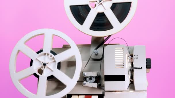 Retro-Rolle mit rotierendem Film auf rosa Studiohintergrund. Altmodischer 8mm-Filmprojektor beim Spielen. Vintage-Filmobjekte, Raritätenkonzept — Stockvideo