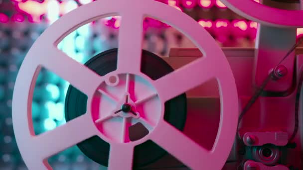 Retro reel with film rotating on sequins kinetic wall, neon light. Old-fashioned 8mm projector playing in decorated room. Vintage objects, cinema, Hollywood concept — Stock Video