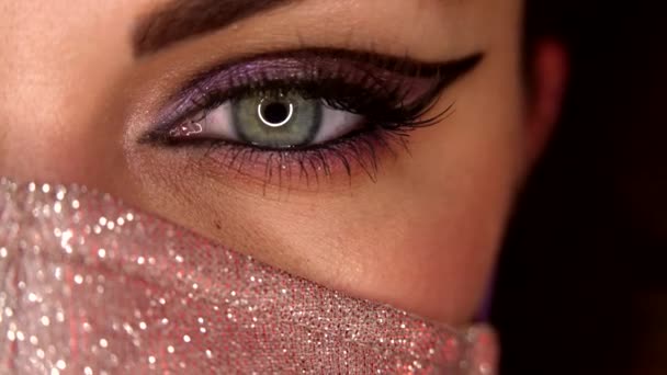 Woman in shimmer protective facial mask. Macro. Glitter eyeshadows and false lashes. Model eye blinking with fancy arrow make-up. Girl, green eye. Pandemic, covid-19 concept. — Stock Video