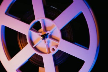 Retro eski moda 8 mm 'lik projektör kaset filmiyle makara oynuyor. Renkli ışık altında dönen bobin yakın plan. Eski nesneler, eğlence, nostalji, festival ekipmanları