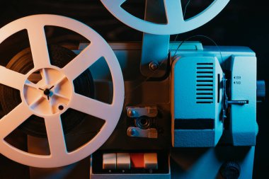 Dönüşümlü beyaz makaralar. Analog oynatıcı. Eski moda 8mm film projektörü ev sinemasında karanlıkta oynuyor. Eski nesneler, sinema, sinematograf konsepti