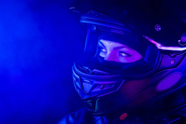 一个戴着封闭摩托车头盔的自信的骑摩托车的女人的画像。夜间在蓝色霓虹灯下的年轻司机骑自行车。复制空间. — 图库照片
