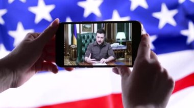 Nisan 2022 - Chicago, ABD. Başkan Volodymyr Zelensky 'nin çevrimiçi konuşmasını Amerikan bayrağı arka planında akıllı telefondan izliyorum. Haberler. Rus saldırganlığı. Savaş tehdidi..