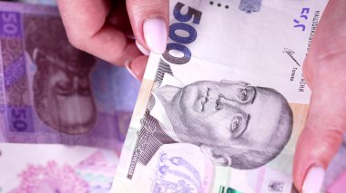 Kadın, UAH nakit paralarını arka planda sayıyor. Piyangoyu kazanan kişi, pazarlıktan gelir. Ellerinde yeni banknotlar.