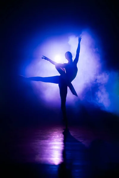 Силуэт балерины в студии с фиолетовым неоновым красочным светом. Молодая женщина танцует в классическом платье из пачки. Изящество и нежность в каждом движении. — стоковое фото