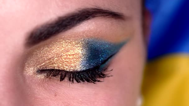 Makro pohled na ženské oko s modrým žlutým lesklým make-upem. Dámo, zelená rohovka s kulatým odrazem. Ukrajinský model na pozadí vlajky. — Stock video