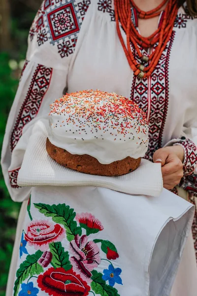 Ukrainka trzyma w rękach tort wielkanocny. Pani w hafcie vyshivanka sukienka na tle natury. Symbol wakacji, religii i tradycji. — Zdjęcie stockowe