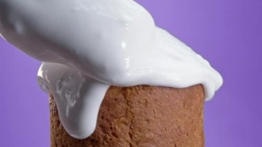 Close-up of rotating Easter cake, decoration with white glaze, traditional bakery. Spring christian religious holiday. Delicious homemade festive sweets. Violet background.