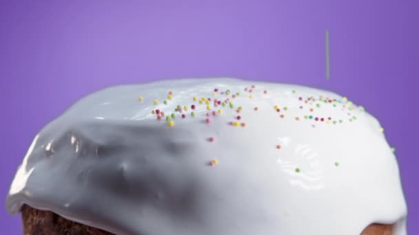 Rotating Easter cake, decoration with white glaze and colorful sugar sprinkling, traditional bakery. Spring christian religious holiday. Delicious homemade festive sweets. Violet background. — Vídeo de Stock