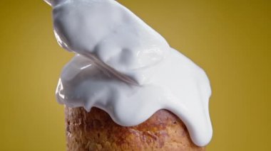 Close-up of rotating Easter cake, decoration with white glaze, traditional bakery. Spring christian religious holiday. Delicious homemade festive sweets. Yellow background.