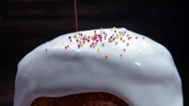 Rotating Easter cake, decoration with white glaze and colorful sugar sprinkling, traditional bakery. Spring christian religious holiday. Delicious homemade festive sweets. Black background.