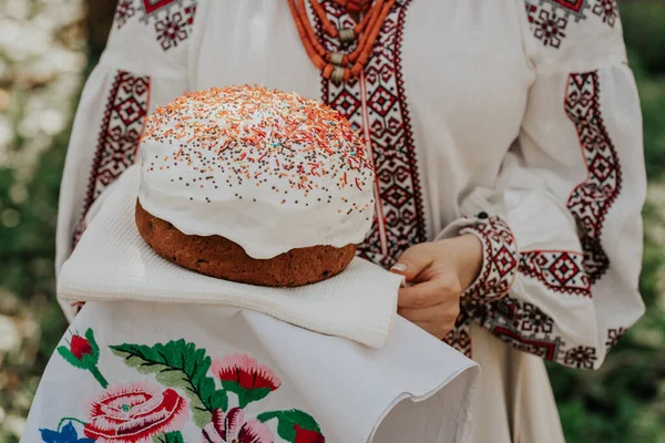 Ukrainka trzyma w rękach tort wielkanocny. Pani w hafcie vyshivanka sukienka na tle natury. Symbol wakacji, religii i tradycji. — Zdjęcie stockowe