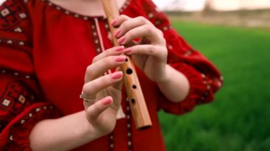 Woman playing woodwind wooden flute - ukrainian sopilka outdoors. Folk music concept. Musical instrument. Lady in traditional embroidered shirt - red Vyshyvanka.