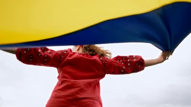 Happy ukrainian woman spinning around with national flag on sky background. Lady in red embroidery Vyshyvanka and flowers wreath. Ukraine freedom, patriot symbol, victory in war. — стокове відео