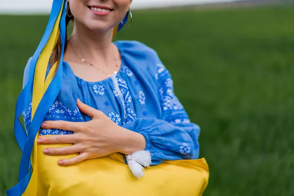 Улыбающаяся украинка с национальным флагом на зеленом фоне поля. Девушка в голубой вышивке. Украина, независимость, свобода, патриотический символ, победа в войне. — стоковое фото