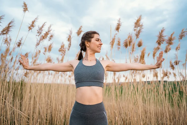 Avrupalı bir kadın sazlıklar üzerinde yoga egzersizi yapıyor. Yazın açık havada konsantre kız eğitimi. Pastel renkler, doğayla bütünlük, denge, yaşam tarzı konsepti.