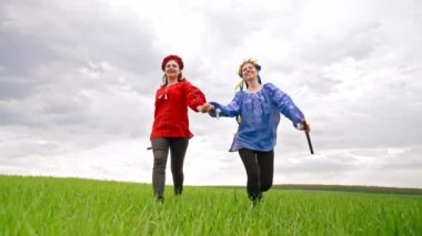 Happy women running, holding flute - ukrainian sopilka in hands. Green field. Portrait of young friends in embroidery vyshyvanka - national blouse. Ukraine, friendship, ethnic music concept.