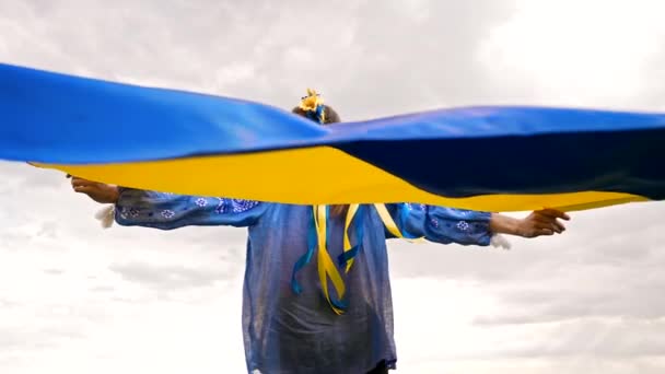 Gökyüzünde ulusal bayrağı olan gülümseyen Ukraynalı kadın. Mavi işlemeli genç bayan portresi vyshyvanka. Ukrayna, bağımsızlık, özgürlük, vatanseverlik sembolü, savaşta zafer. — Stok video