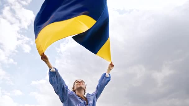 Smiling ukrainian woman with national flag on sky background. Portrait of young lady in blue embroidery vyshyvanka. Ukraine, freedom, patriot symbol, victory in war. — Stockvideo