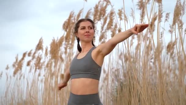 European woman doing yoga exercise on reed natural background. Concentrated girl training at summer outdoors. Pastel colors, unity with nature, balance, lifestyle concept. — Stockvideo